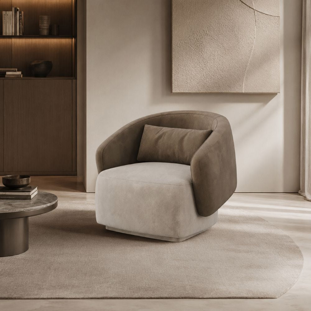 A modern barrel-style accent chair upholstered in light beige and taupe velvet, placed on a neutral rug in a minimalist, warm-toned living room setting.