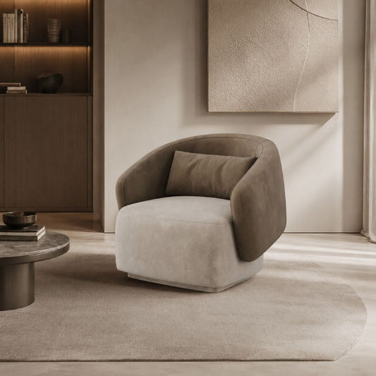 A modern barrel-style accent chair upholstered in light beige and taupe velvet, placed on a neutral rug in a minimalist, warm-toned living room setting.