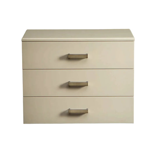 A three-drawer nightstand or storage cabinet in a warm cream-beige finish with slim metallic drawer pulls, shown against a plain white background.